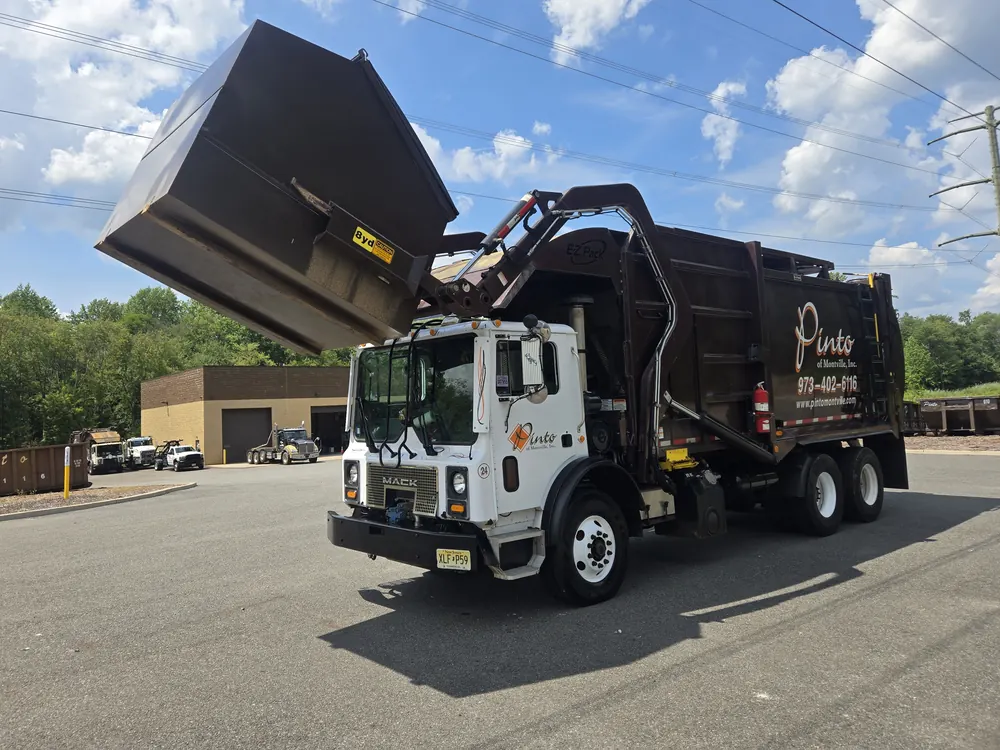 A Pinto of Montville front-load truck lifting a commercial container over its cab, outside the company building