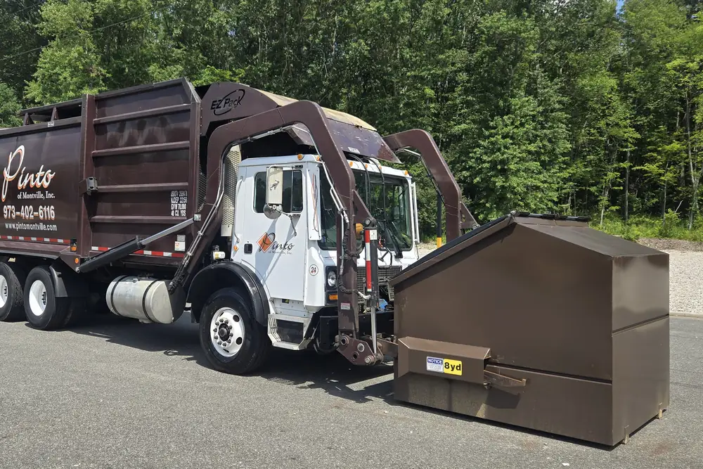 A Pinto of Montville front-load truck parked beside a commercial container