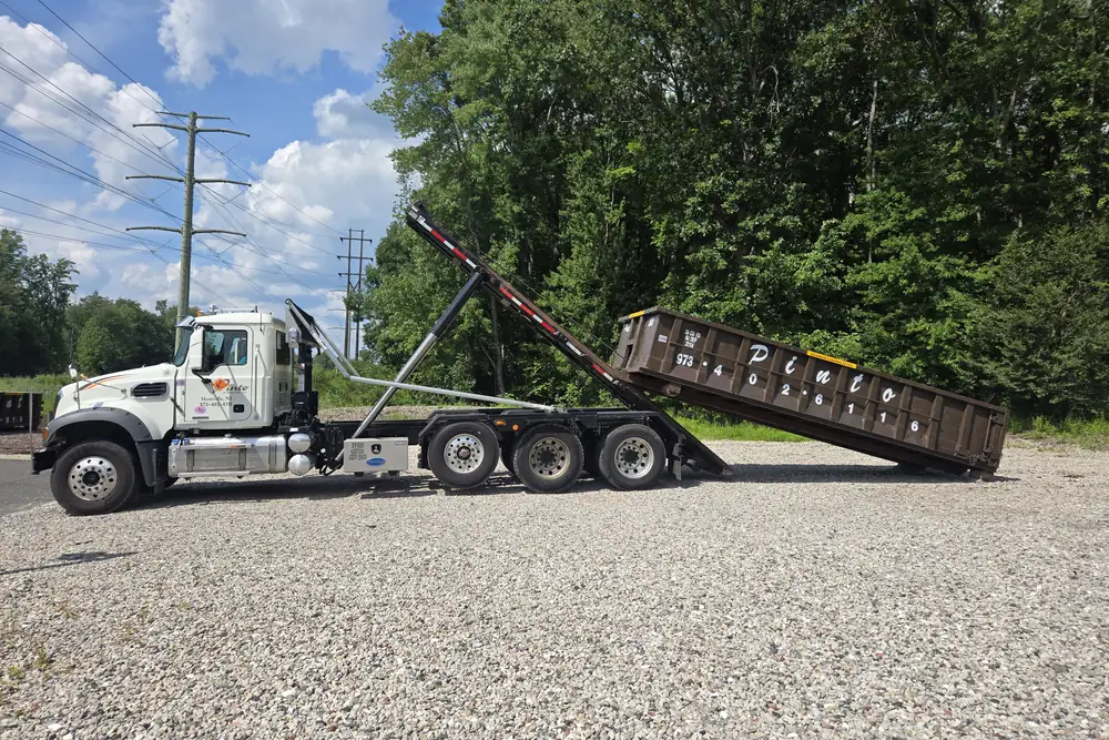 A Pinto of Montville roll-off truck lowering a dumpster into place