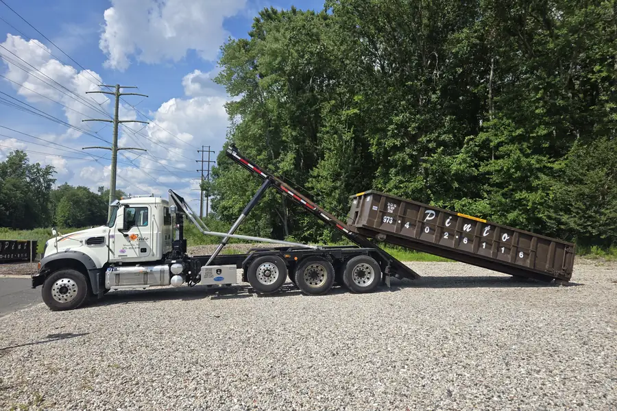A Pinto of Montville roll-off truck lowering a dumpster to the ground